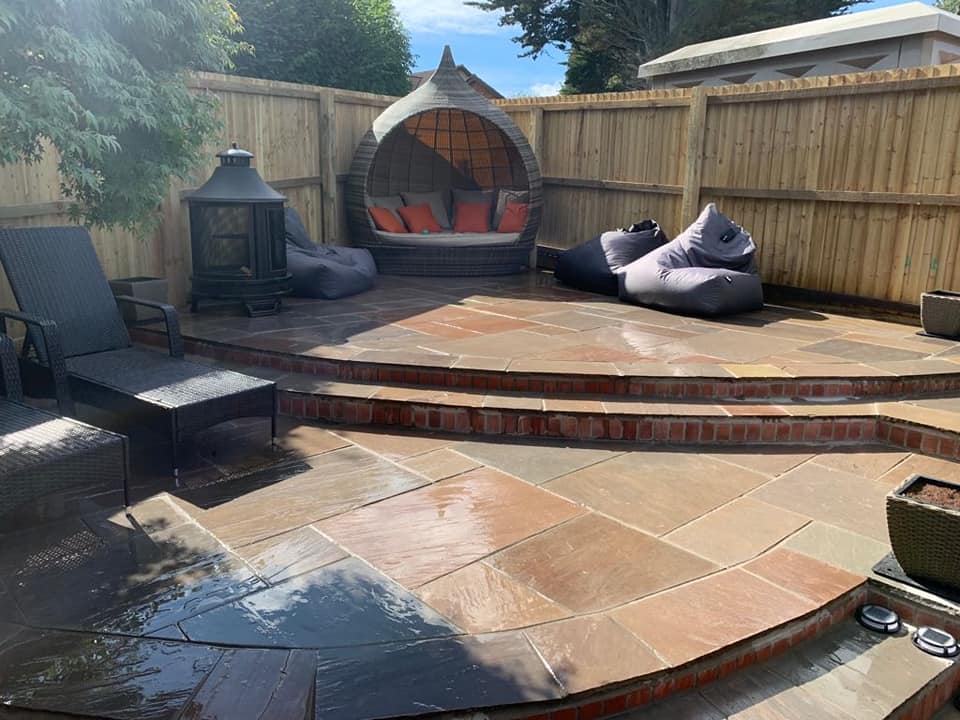 Two-tiered sandstone patio with curved steps and brick risers, with a hanging chair pod and fire pit on the upper level