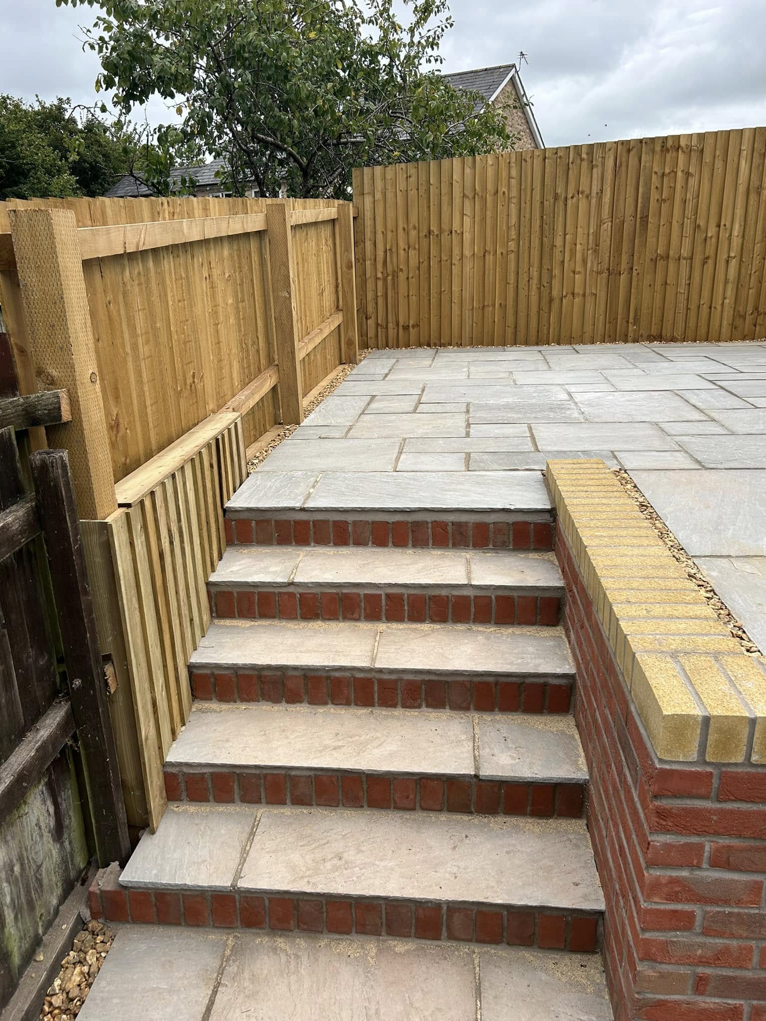 Brick-faced garden steps rising onto a fresh Indian sandstone patio with timber fencing in the background