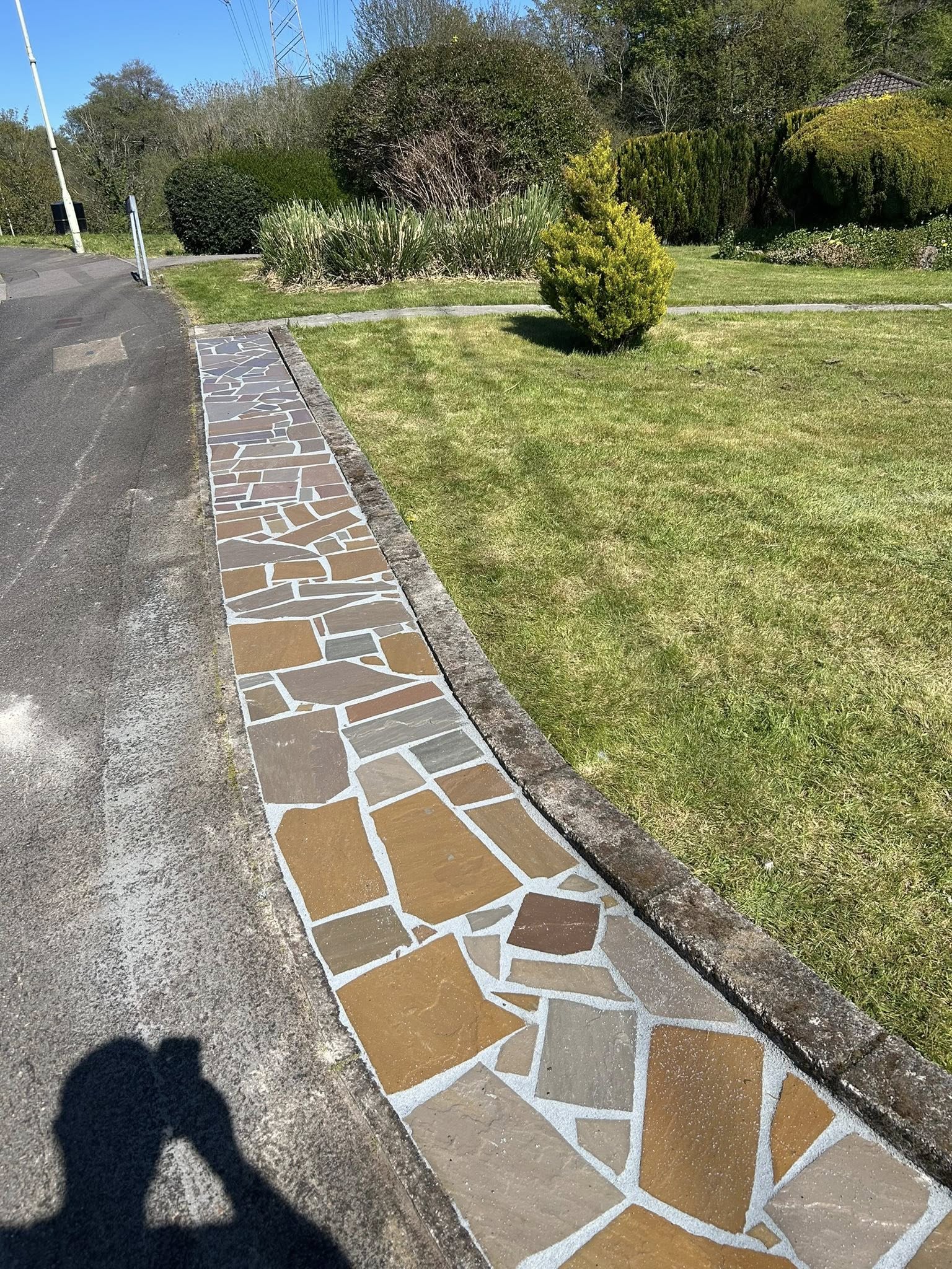 Hand-laid crazy paving pathway running alongside a green lawn under a clear blue sky in South Wales